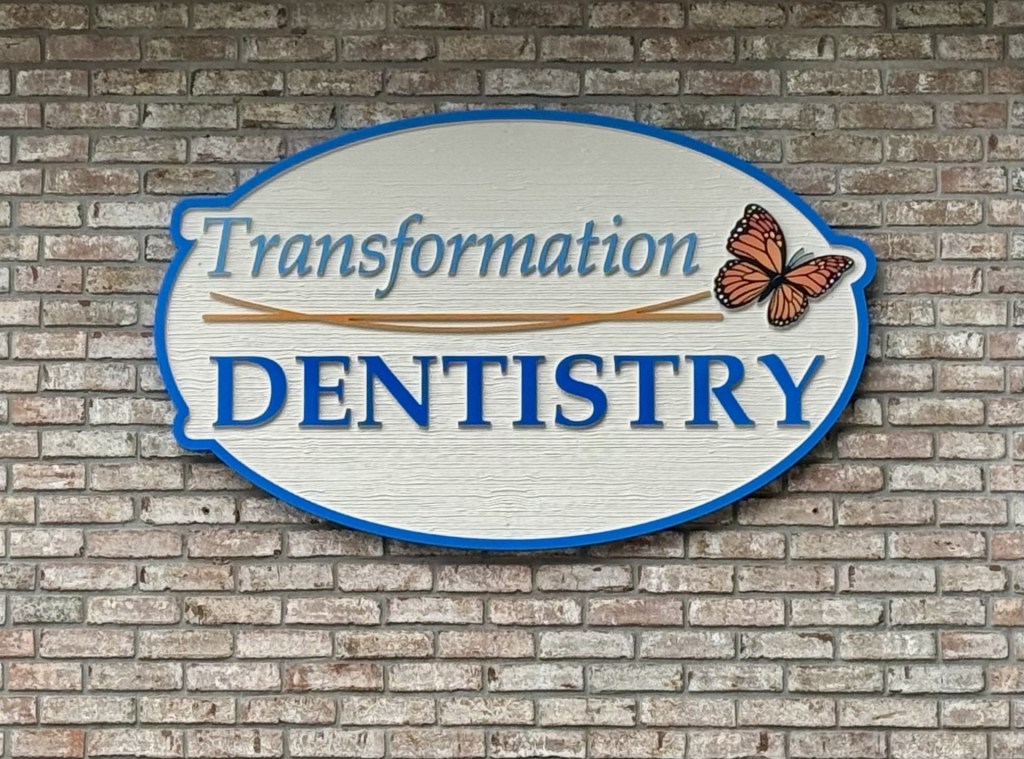 Transformation Dentistry sign with butterfly logo mounted on brick wall