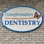 Transformation Dentistry sign with butterfly logo mounted on brick wall
